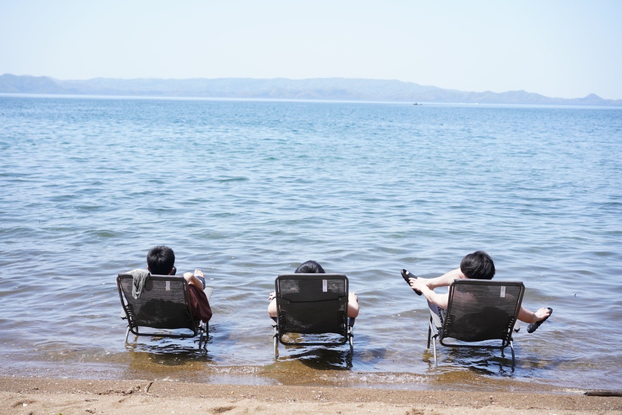 湖の中に置いたチェアで外気浴をする3人